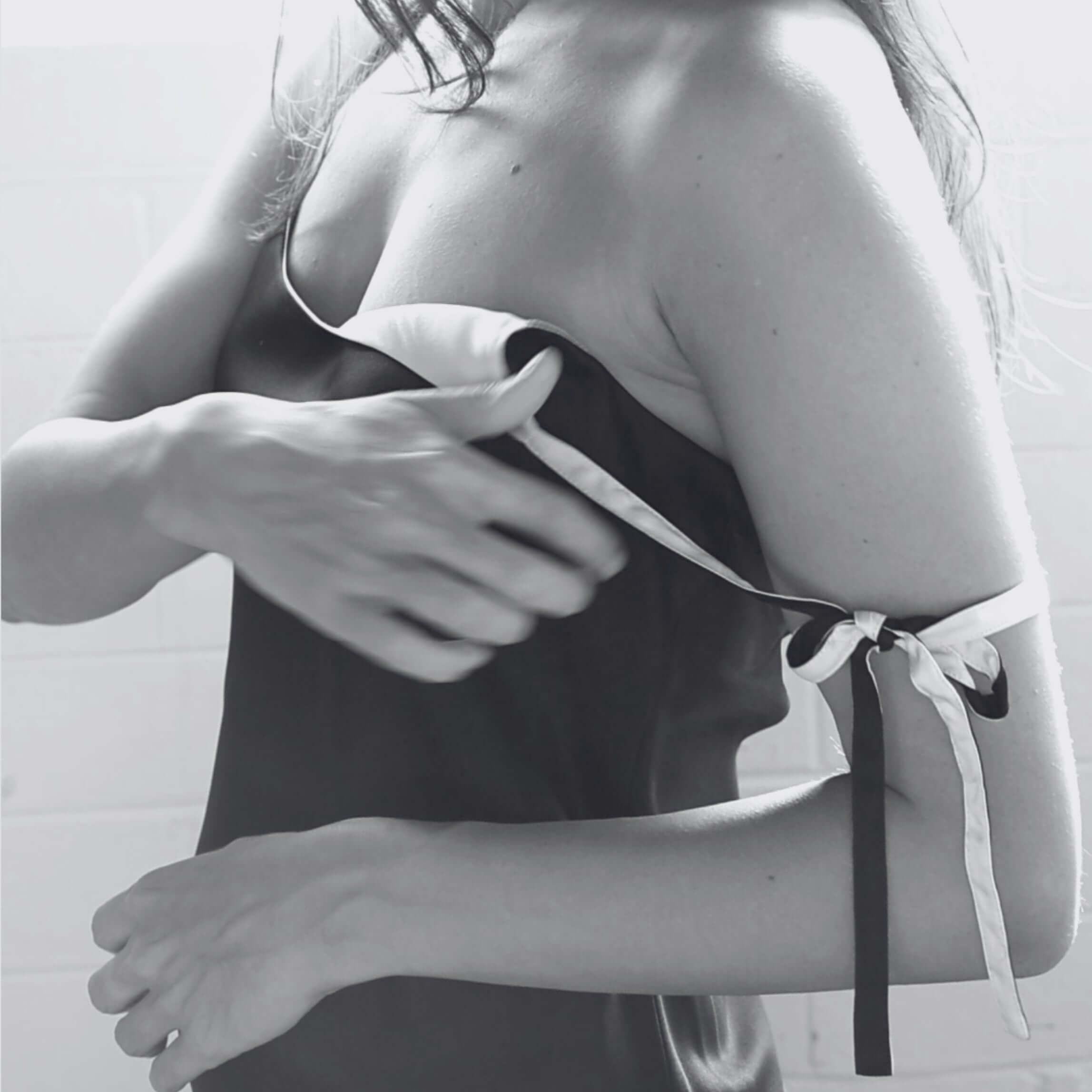 Close-up black and white photo of a woman adjusting the delicate silk tie-strap on the shoulder of The Sonnet Slip.